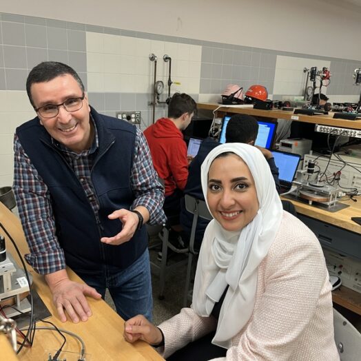 Kamal Youcef-Toumi and Amira Alazmi pose in a bench lab filled with technical equipment